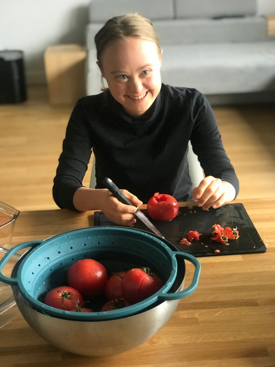 Uśmiechnięta Maja. krojąca czerwonego pomidora.